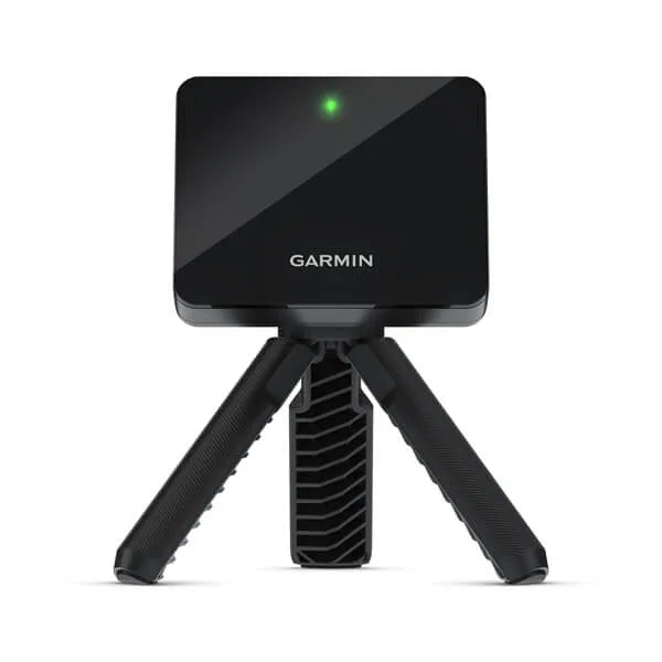 A Garmin Approach R10 Portabe Golf Launch Monitor showing a black rectangular face with a green light, white letters and balanced on a black tripod.